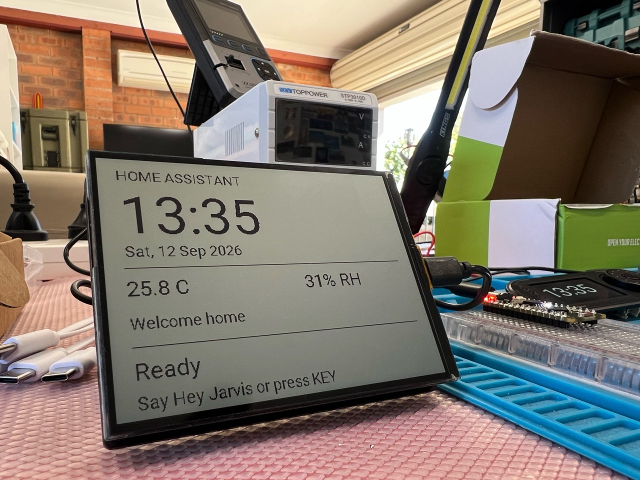 Waveshare reflective LCD on the workbench, displaying a Home Assistant clock, temperature, humidity and a welcome message
