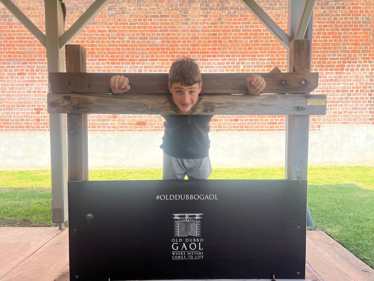 A boy posing in the stocks at the Old Dubbo Gaol