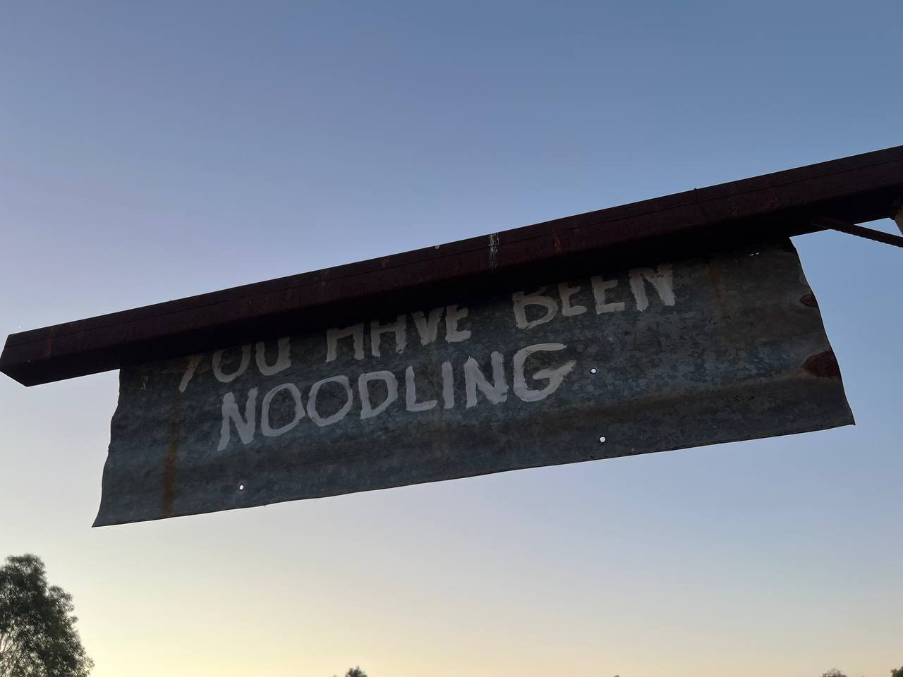 A hand-painted sign reading YOU HAVE BEEN NOODLING against the evening sky