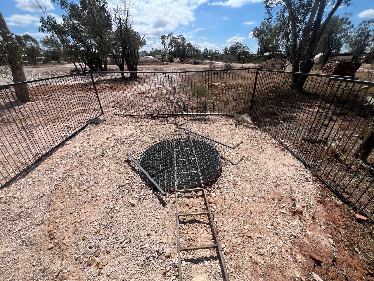 A fenced and grated mine shaft on the opal fields, with a ladder leading down