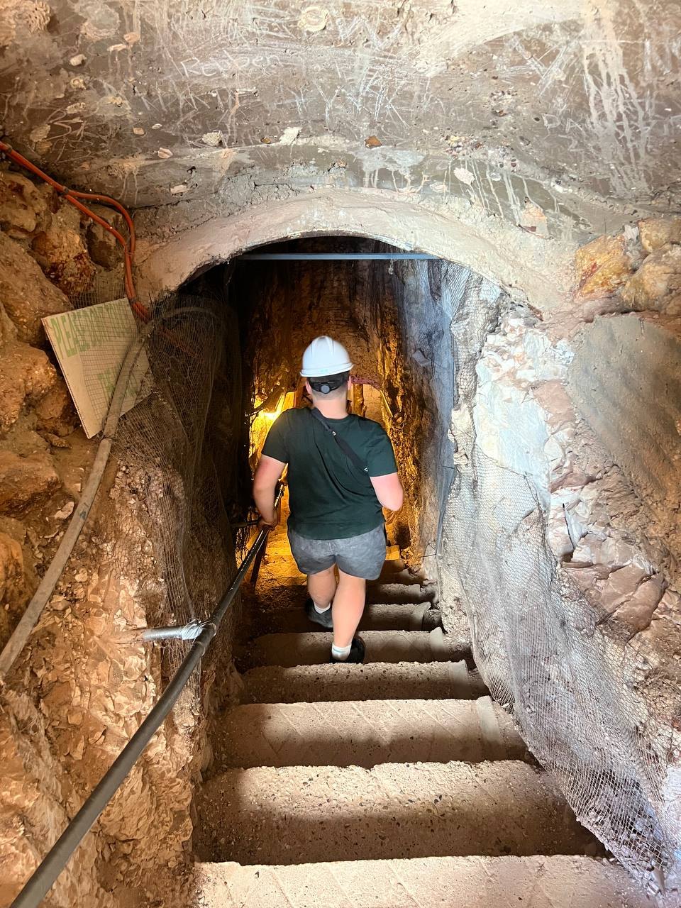 Heading down a narrow stone staircase into the mine, rock walls lined with safety mesh
