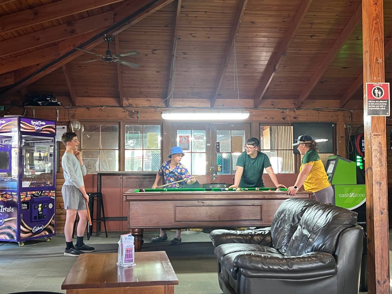 Four of the kids around a pool table in a pub's wood-panelled games room, one lining up a shot