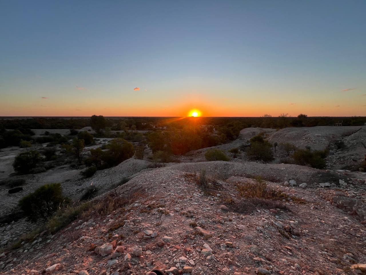 The sun low on the horizon over the flat treeline, the gravelly ridges lit orange