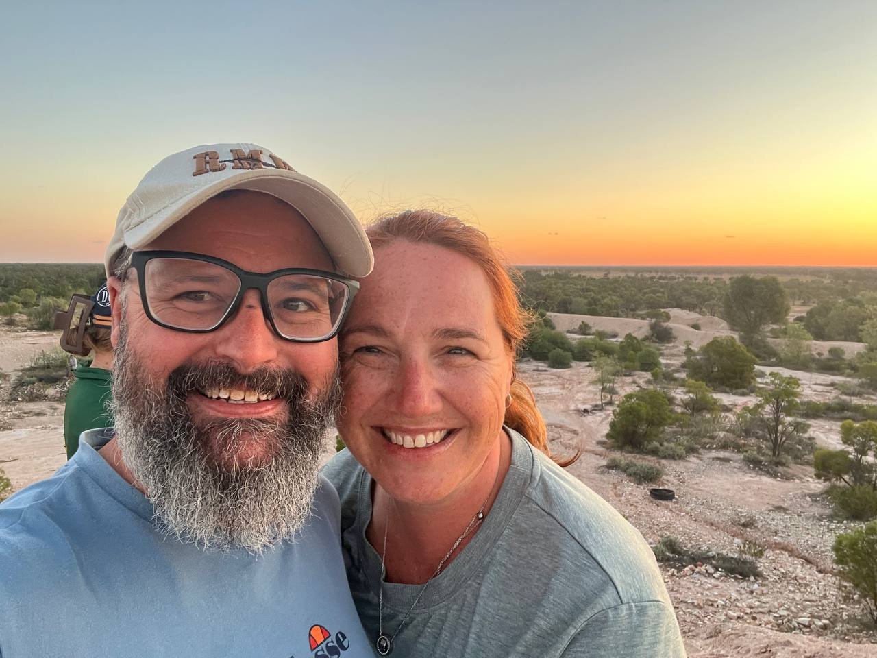 A couple take a selfie with the sunset over the scrub behind them