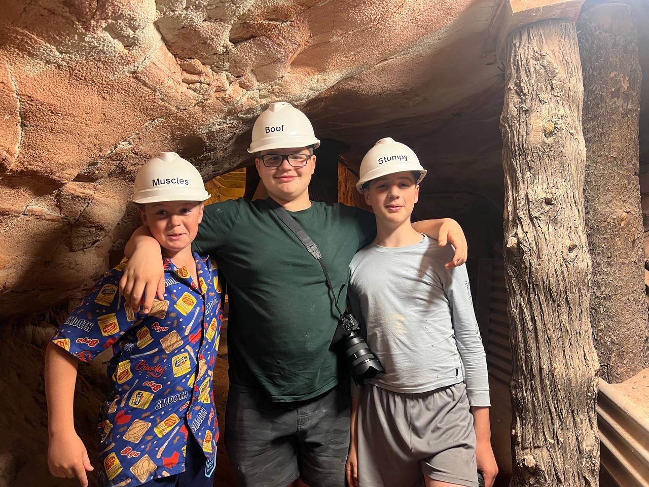 Three of the party underground in white hard hats labelled Muscles, Boof, and Stumpy